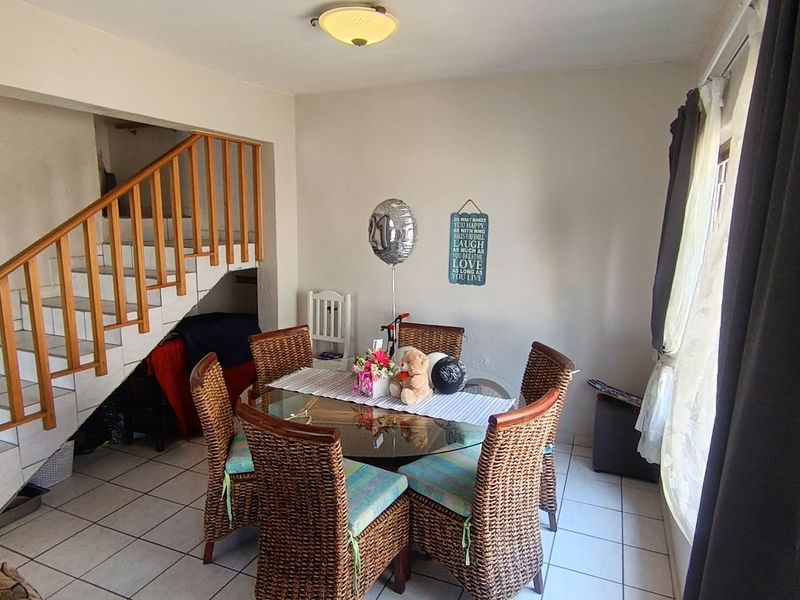 Dining area featuring tiled flooring and an open wooden staircase, providing a functional space for meals.