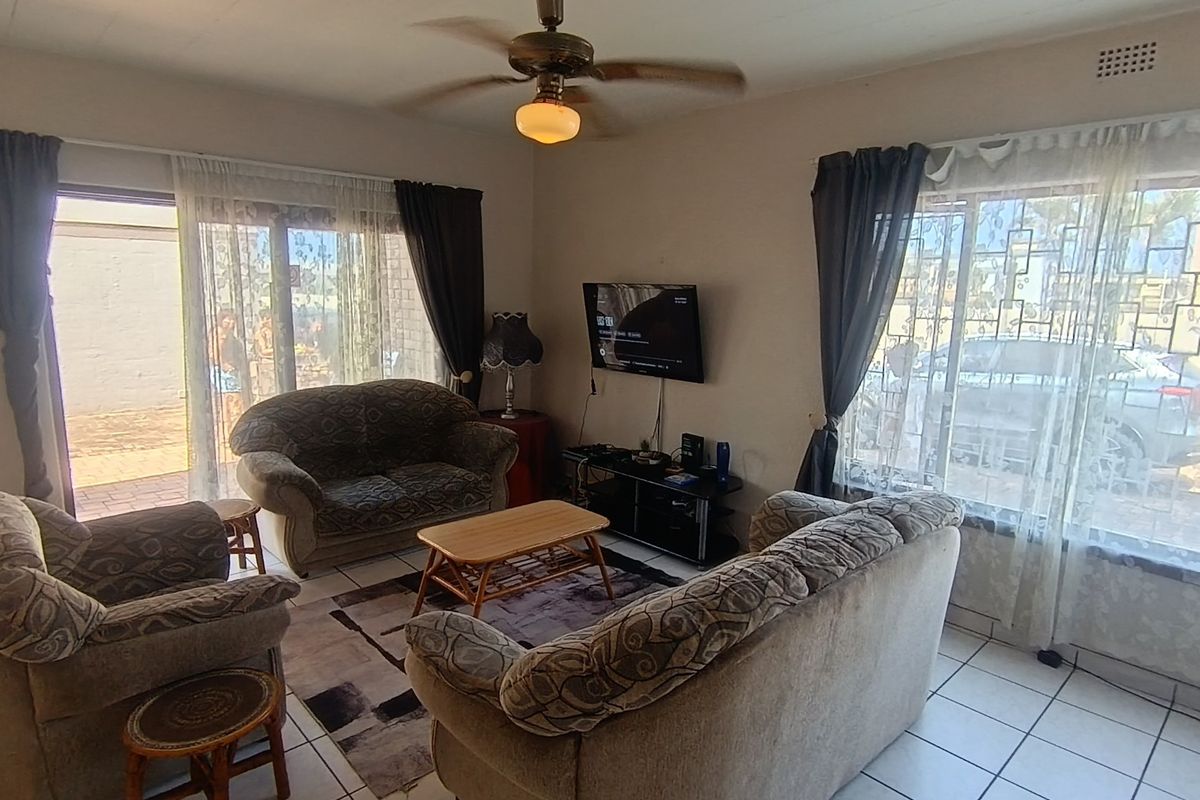 A functional living room featuring tiled flooring, a ceiling fan, and large windows providing natural light with access to an outdoor patio area.
