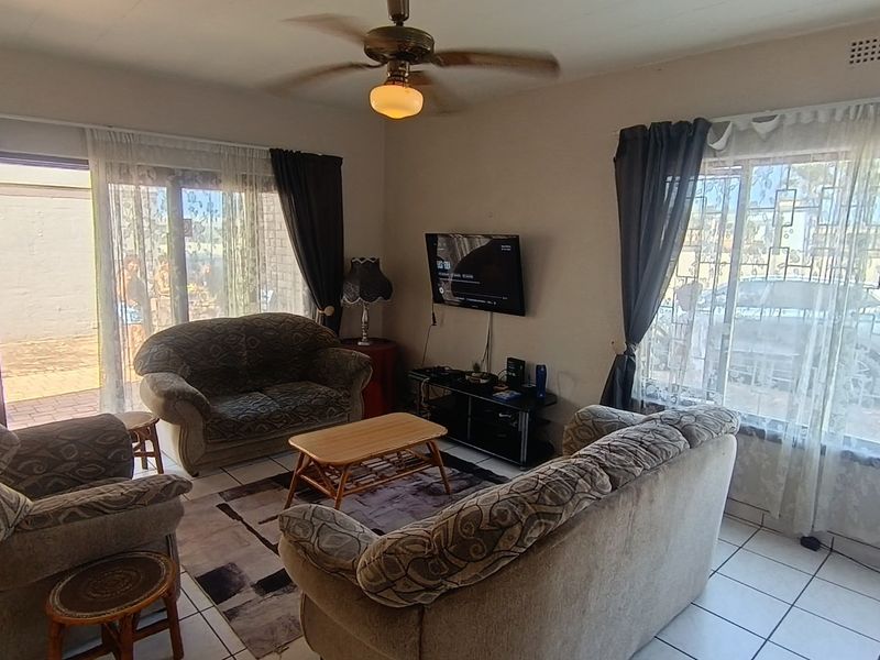 A functional living room featuring tiled flooring, a ceiling fan, and large windows providing natural light with access to an outdoor patio area.
