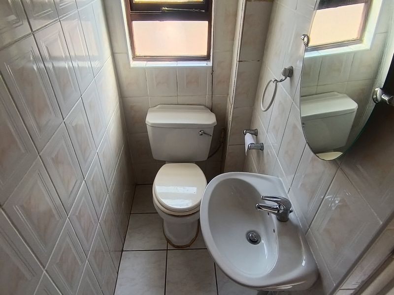 A compact bathroom featuring a standard toilet, wall-mounted washbasin, and full-height wall tiling.