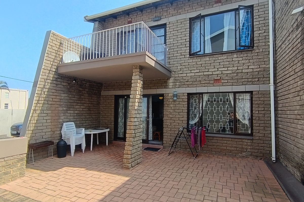Rear view of the property featuring a paved patio area, a balcony above, and brick facade construction with security bars on windows.