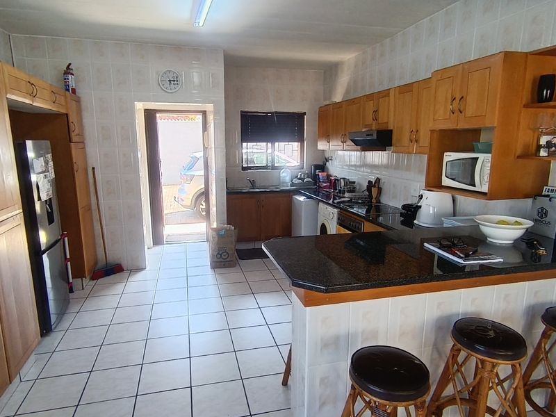 A functional kitchen featuring wooden cabinetry, granite countertops, a breakfast bar, and tiled finishes throughout, with direct access to the exterior.