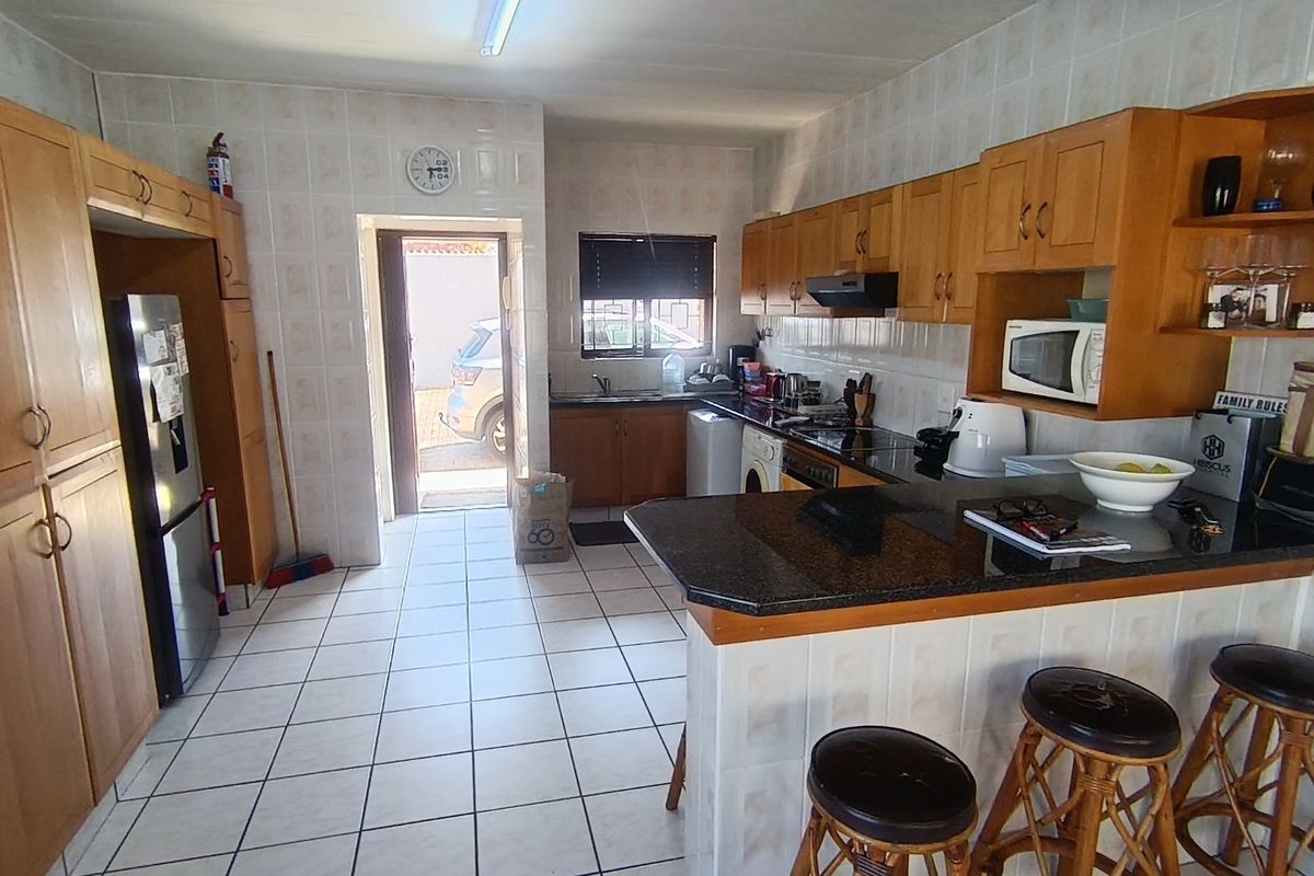 A functional kitchen featuring wooden cabinetry, granite countertops, a breakfast bar, and tiled finishes throughout, with direct access to the exterior.