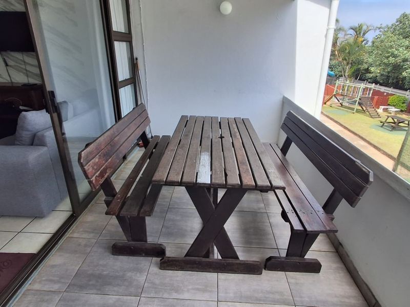 A covered patio area featuring tiled flooring and sliding glass door access, overlooking a communal garden and play area.