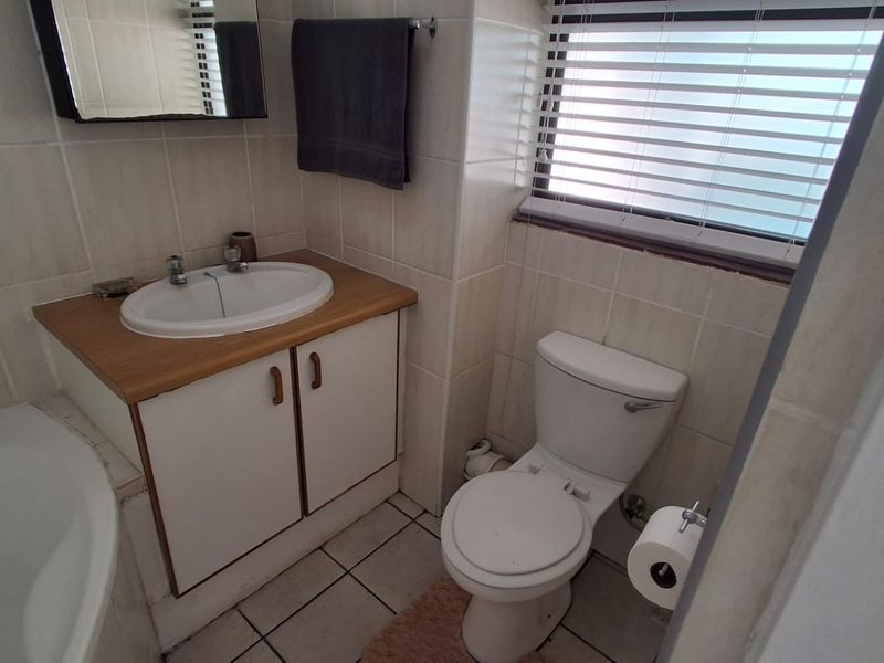 A functional bathroom featuring a vanity cabinet with a basin, a standard toilet, and tiled finishes throughout, complemented by natural light from the window.