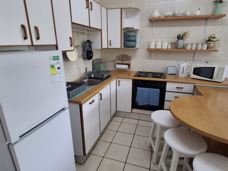 A functional kitchen featuring white cabinetry, laminate countertops, tiled backsplash, and integrated cooking appliances with an attached breakfast nook.