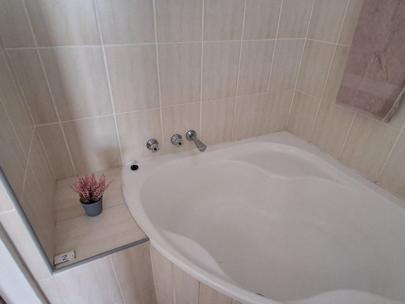 A functional bathroom featuring a built-in bathtub with chrome fixtures and neutral ceramic wall tiling.