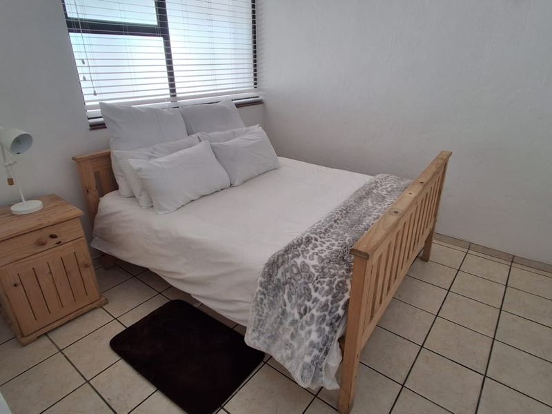A compact bedroom featuring tiled flooring, a built-in wardrobe, and natural light provided by a window with venetian blinds.