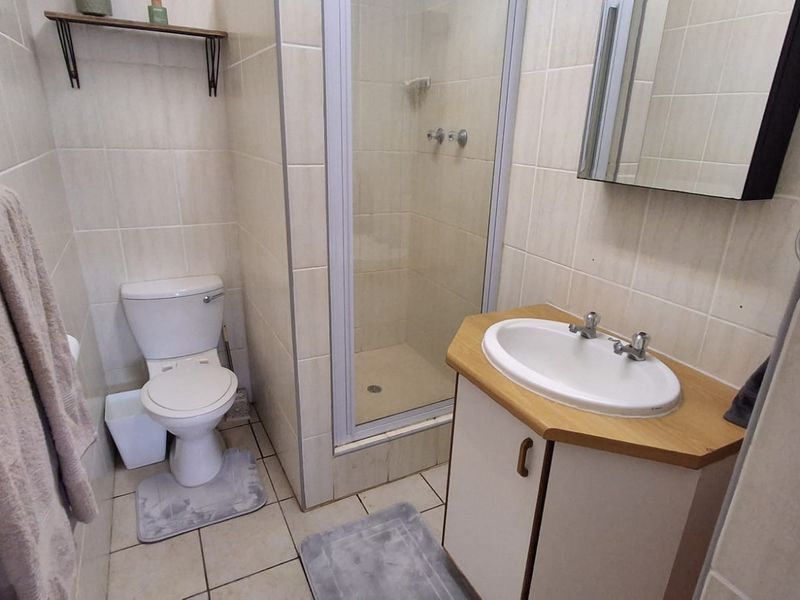 A functional bathroom featuring a shower enclosure, vanity basin with storage, and neutral wall and floor tiling.