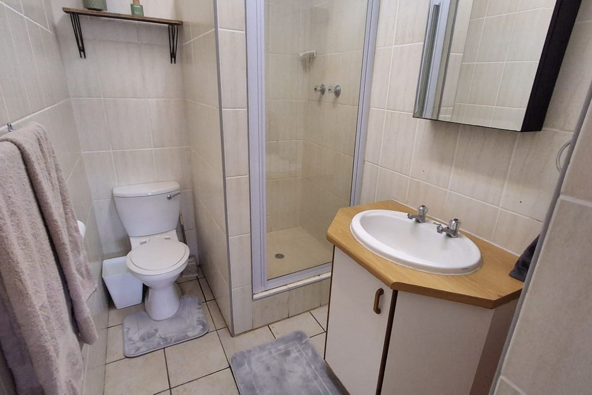 A functional bathroom featuring a shower enclosure, vanity basin with storage, and neutral wall and floor tiling.