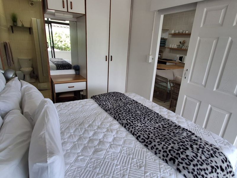 Bedroom featuring built-in wardrobes, a vanity unit, and an adjoining en-suite bathroom, with a sliding door providing access to the kitchen area.