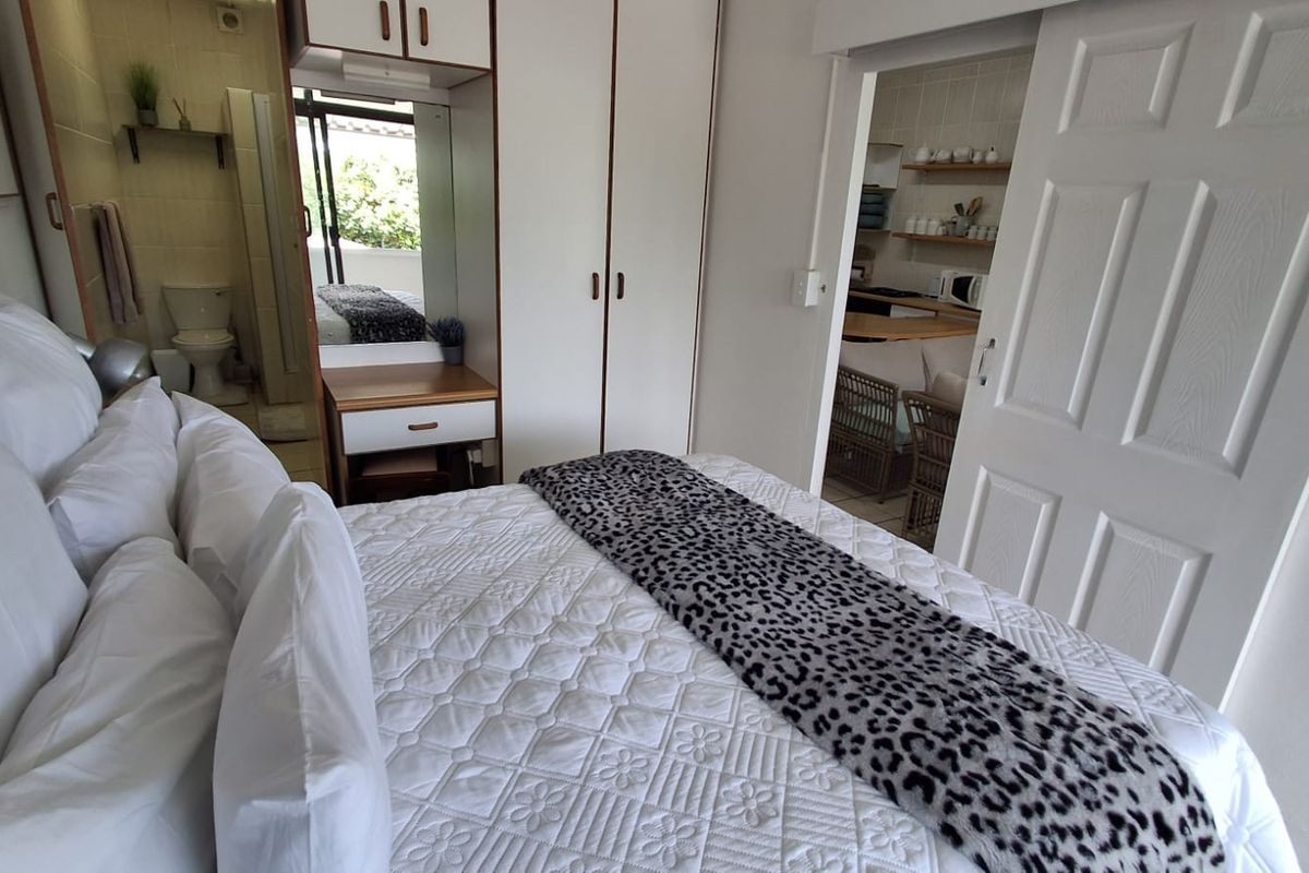 Bedroom featuring built-in wardrobes, a vanity unit, and an adjoining en-suite bathroom, with a sliding door providing access to the kitchen area.