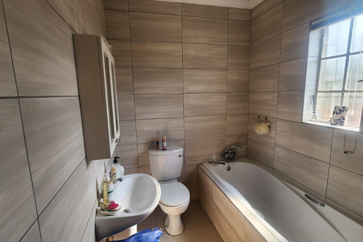 A functional bathroom featuring full-height wall tiling, a pedestal washbasin, a standard toilet, and a built-in bathtub with a window for natural light.