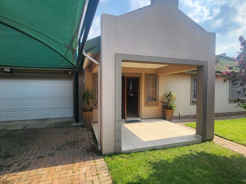 Front entrance of the house featuring a covered patio, paved driveway, and attached garage with a shade sail structure.