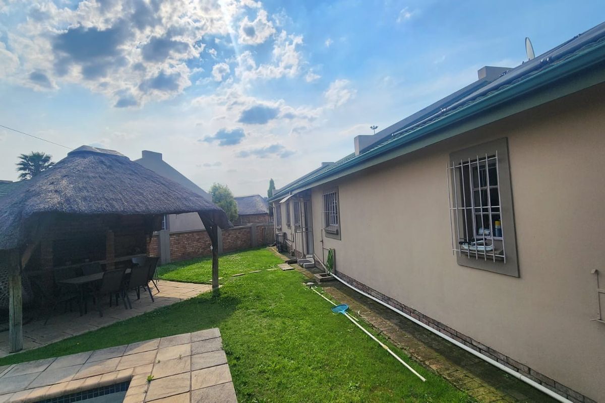 Rear exterior view featuring a lawn, paved patio area with a thatch lapa, and a swimming pool adjacent to the main house structure.