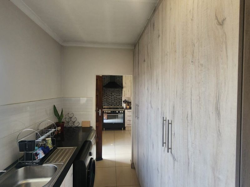 A functional scullery featuring extensive built-in cabinetry, a stainless steel sink with mixer tap, and tiled finishes, providing additional prep and storage space.