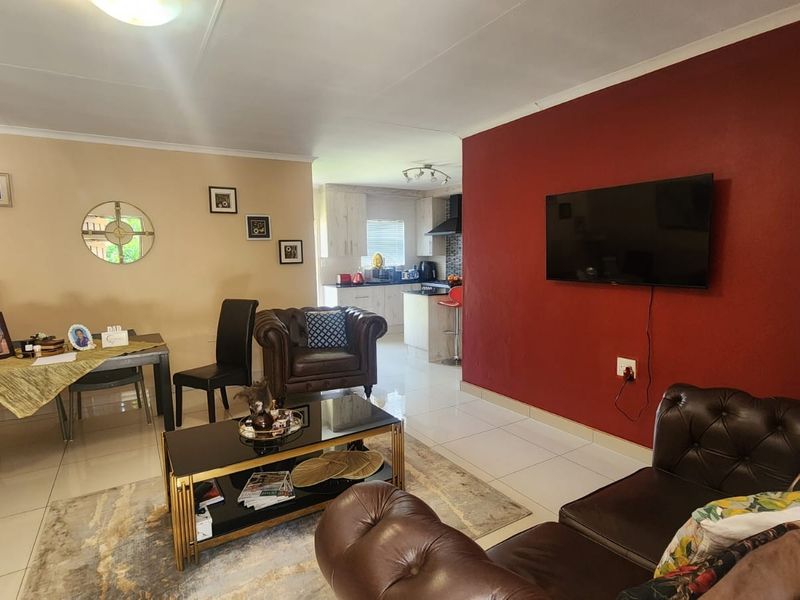 An open-plan living and dining area featuring tiled flooring and a connected kitchen with built-in cabinetry and appliances.