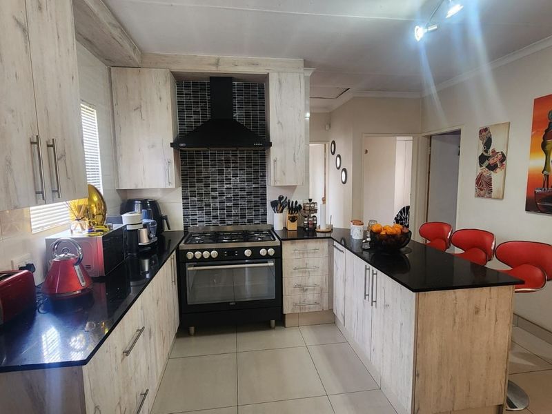 A functional kitchen featuring light wood-grain cabinetry, black granite countertops, a gas hob with extractor fan, and a breakfast bar peninsula.