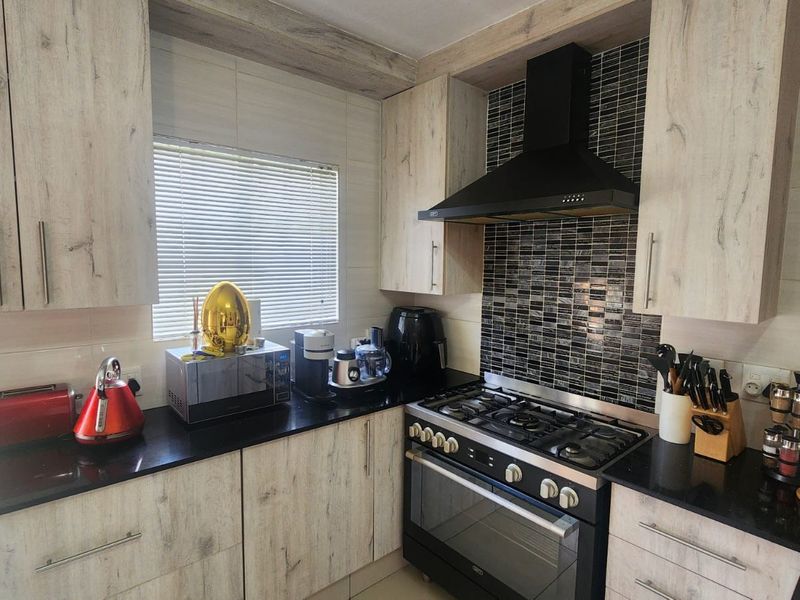 Modern kitchen featuring light wood-grain cabinetry, black granite countertops, a gas stove with extractor fan, and a stylish mosaic tiled backsplash.