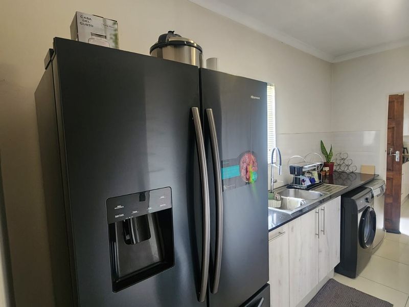 A functional kitchen area featuring built-in cabinetry, a stainless steel sink, and tiled splashbacks, with an adjacent view into a secondary cooking space.