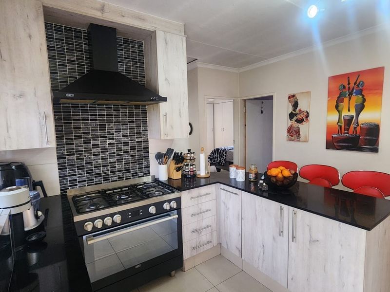 A functional kitchen featuring light wood-grain cabinetry, black granite countertops, a gas stove with extractor fan, and a tiled backsplash with a breakfast bar.