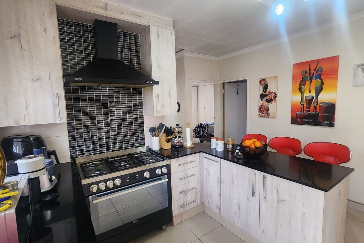 A functional kitchen featuring light wood-grain cabinetry, black granite countertops, a gas stove with extractor fan, and a tiled backsplash with a breakfast bar.