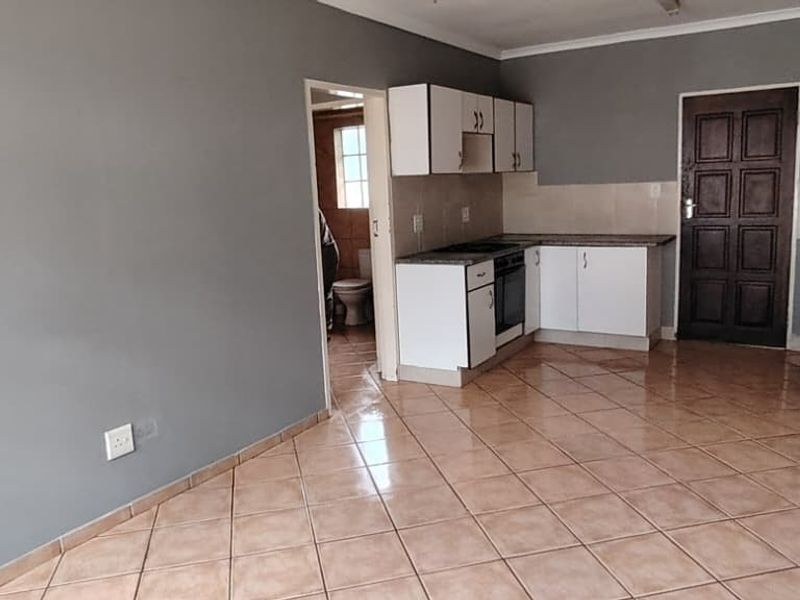 Open-plan living area featuring tiled flooring and a functional kitchen with built-in cabinetry, oven, hob, and sink, with direct access to an adjacent room.