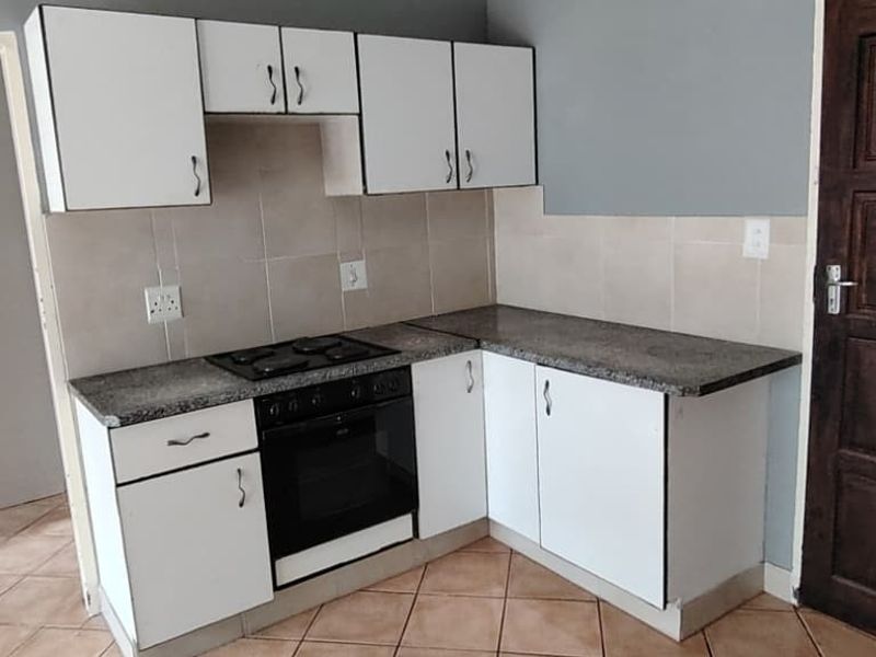 A compact kitchen featuring white built-in cabinetry, granite countertops, an integrated electric hob and oven, and tiled flooring.