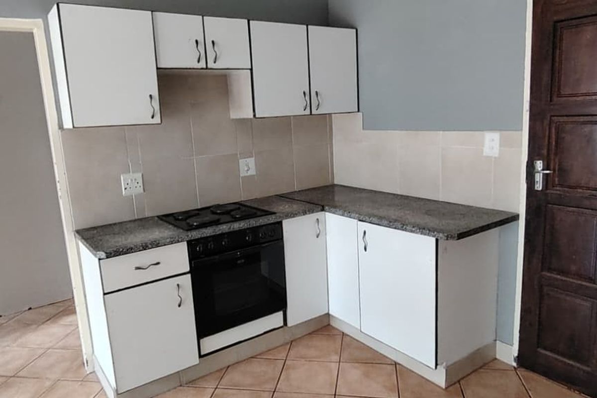 A compact kitchen featuring white built-in cabinetry, granite countertops, an integrated electric hob and oven, and tiled flooring.