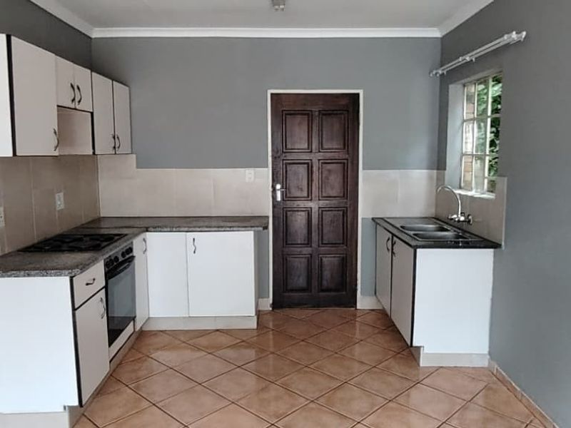 A functional kitchen featuring white cabinetry, granite countertops, a built-in oven and hob, and tiled flooring, with an adjacent view into a bathroom.