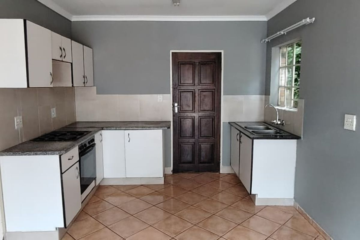 A functional kitchen featuring white cabinetry, granite countertops, a built-in oven and hob, and tiled flooring, with an adjacent view into a bathroom.