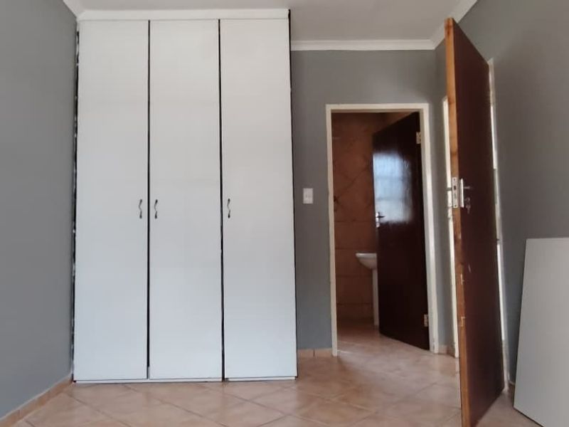 A bedroom featuring tiled flooring, built-in white wardrobes, and direct access to an adjacent bathroom area.