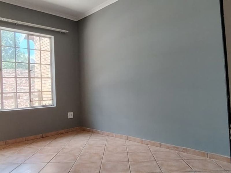 An empty bedroom featuring neutral grey walls, tiled flooring, and a window with security bars, offering a clean and versatile space.