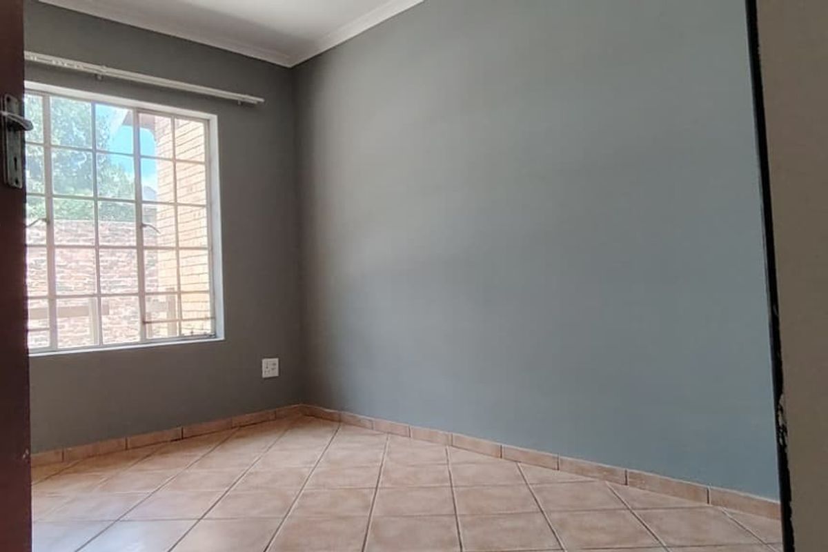 An empty bedroom featuring neutral grey walls, tiled flooring, and a window with security bars, offering a clean and versatile space.