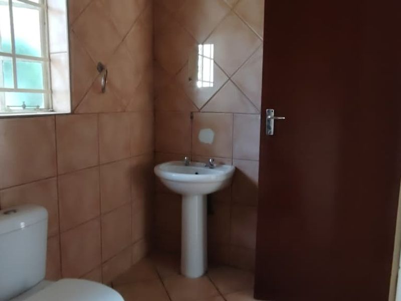 A functional bathroom featuring tiled walls and flooring, a pedestal basin, and a toilet, currently awaiting cosmetic updates and finishing touches.