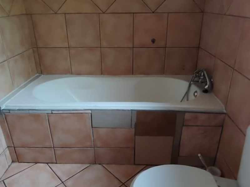 A bathroom featuring a built-in bathtub with tiled surround and a standard toilet, requiring cosmetic updates to the tile finishes.