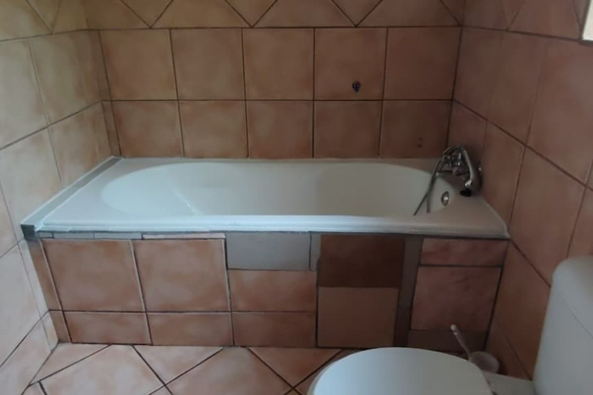 A bathroom featuring a built-in bathtub with tiled surround and a standard toilet, requiring cosmetic updates to the tile finishes.