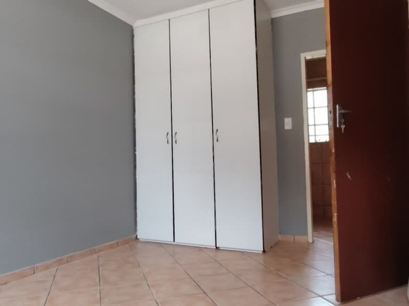 A vacant bedroom featuring neutral grey walls, tiled flooring, and a built-in white wardrobe, offering a clean canvas for personalization.