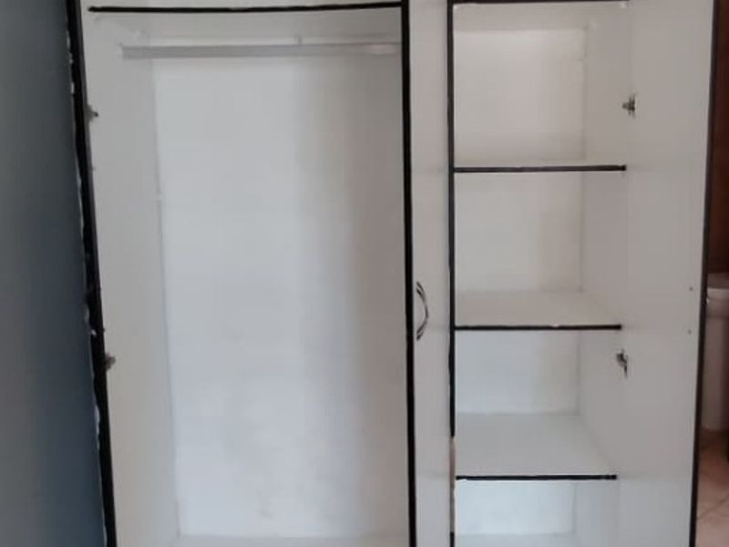 A bedroom featuring a built-in wardrobe with shelving and hanging space, finished with tiled flooring.