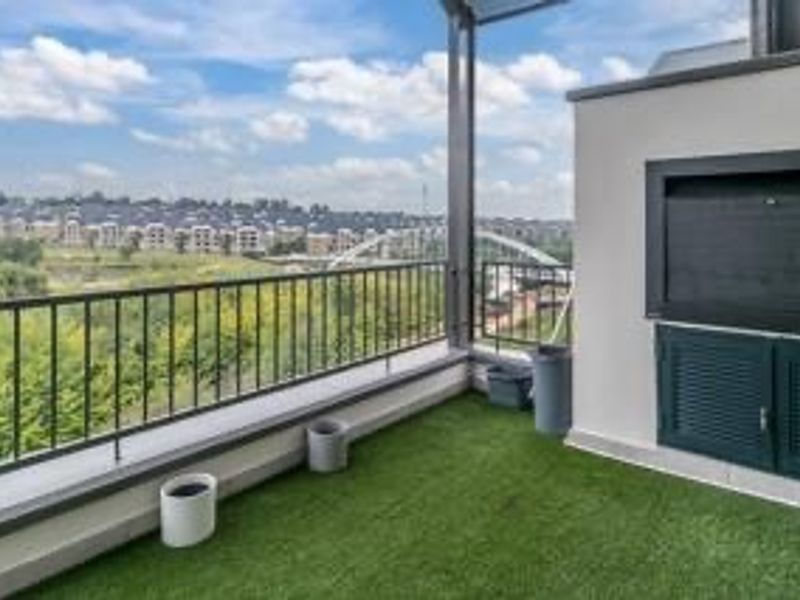 Spacious penthouse balcony featuring a built-in braai, metal balustrade, and artificial grass, offering expansive views of the surrounding area.