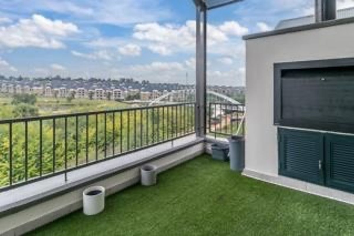 Spacious penthouse balcony featuring a built-in braai, metal balustrade, and artificial grass, offering expansive views of the surrounding area.