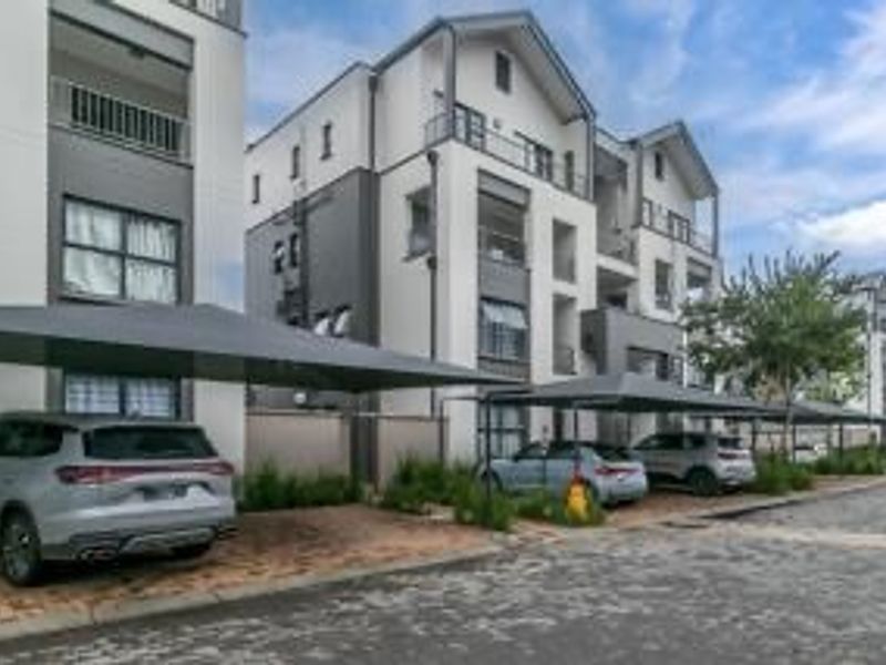 Exterior view of a modern multi-story penthouse complex featuring paved parking areas with shade cloth carports and private balconies.