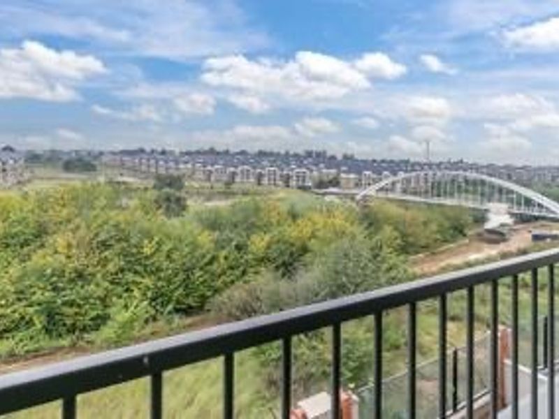 Elevated panoramic view overlooking a green landscape, bridge, and surrounding residential development from a balcony with a metal balustrade.