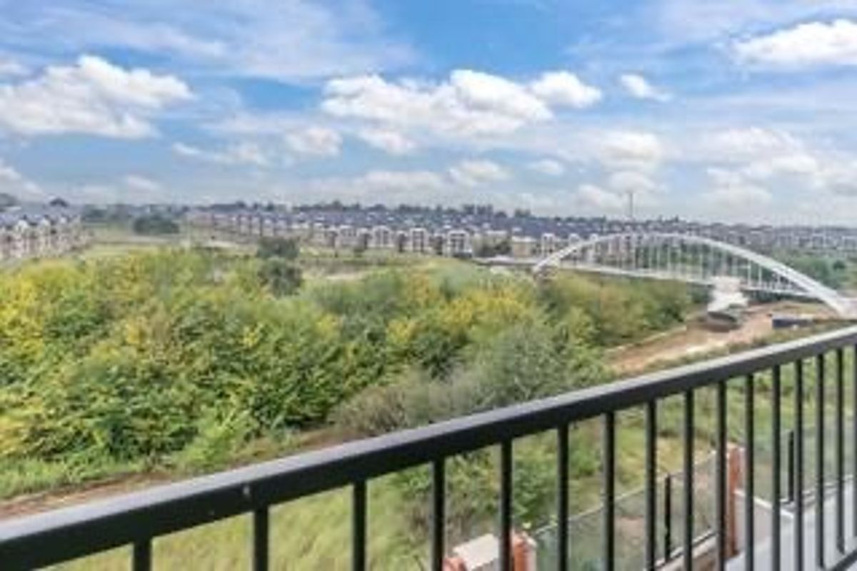 Elevated panoramic view overlooking a green landscape, bridge, and surrounding residential development from a balcony with a metal balustrade.