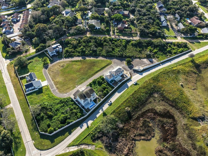 An aerial view of a residential vacant land plot situated within a developed estate, featuring established boundary walls and access to paved roads.