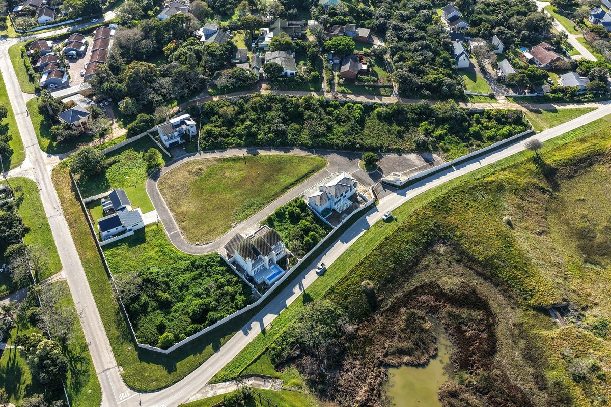 An aerial view of a residential vacant land plot situated within a developed estate, featuring established boundary walls and access to paved roads.