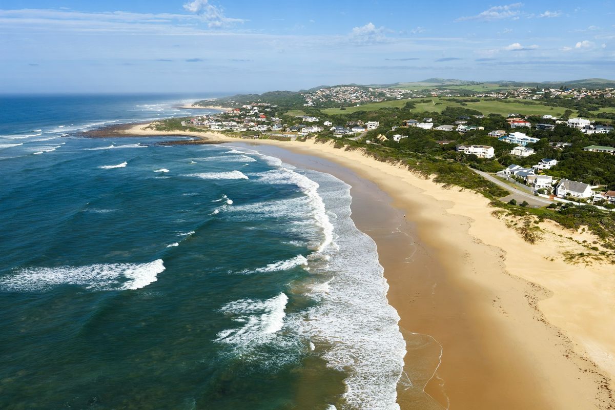 An aerial view of the coastal landscape, showcasing the expansive sandy beach, ocean waves, and surrounding residential area.