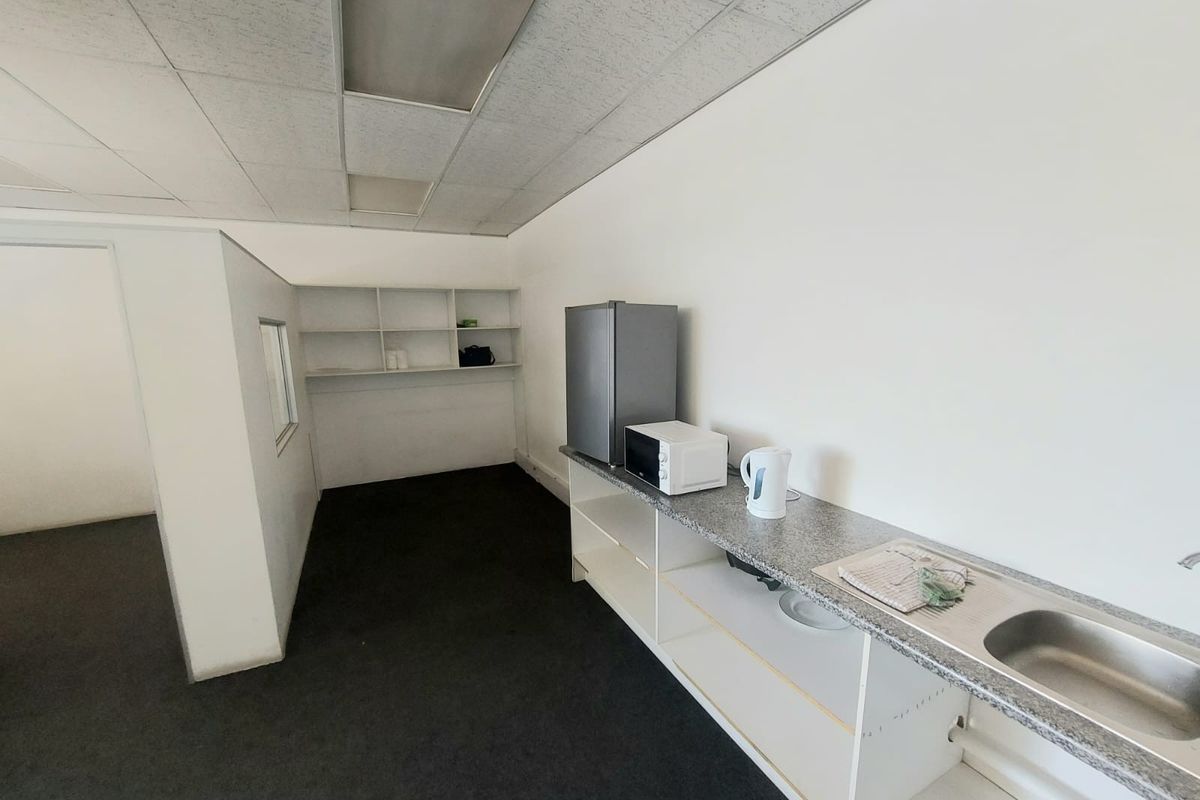 A functional kitchenette area featuring a stainless steel sink, laminate countertop, and built-in shelving, suitable for office or industrial utility use.