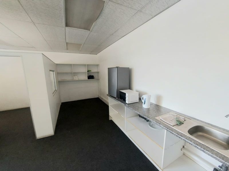 A functional kitchenette area featuring a stainless steel sink, laminate countertop, and built-in shelving, suitable for office or industrial utility use.