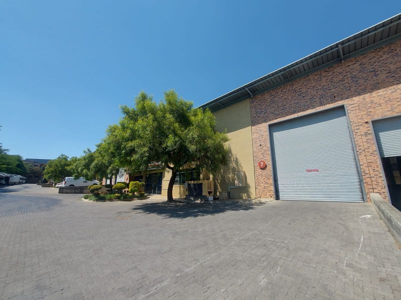 Industrial warehouse exterior featuring a large roller shutter door, brick facade, and paved driveway access.
